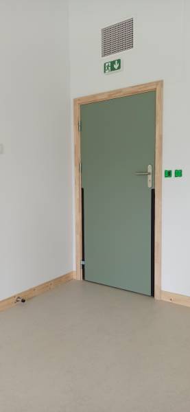 Bloc-porte technique stratifié avec poignée PMR, signalétique de sécurité et plinthe en sapin, assurant accessibilité et sécurité dans un environnement scolaire.